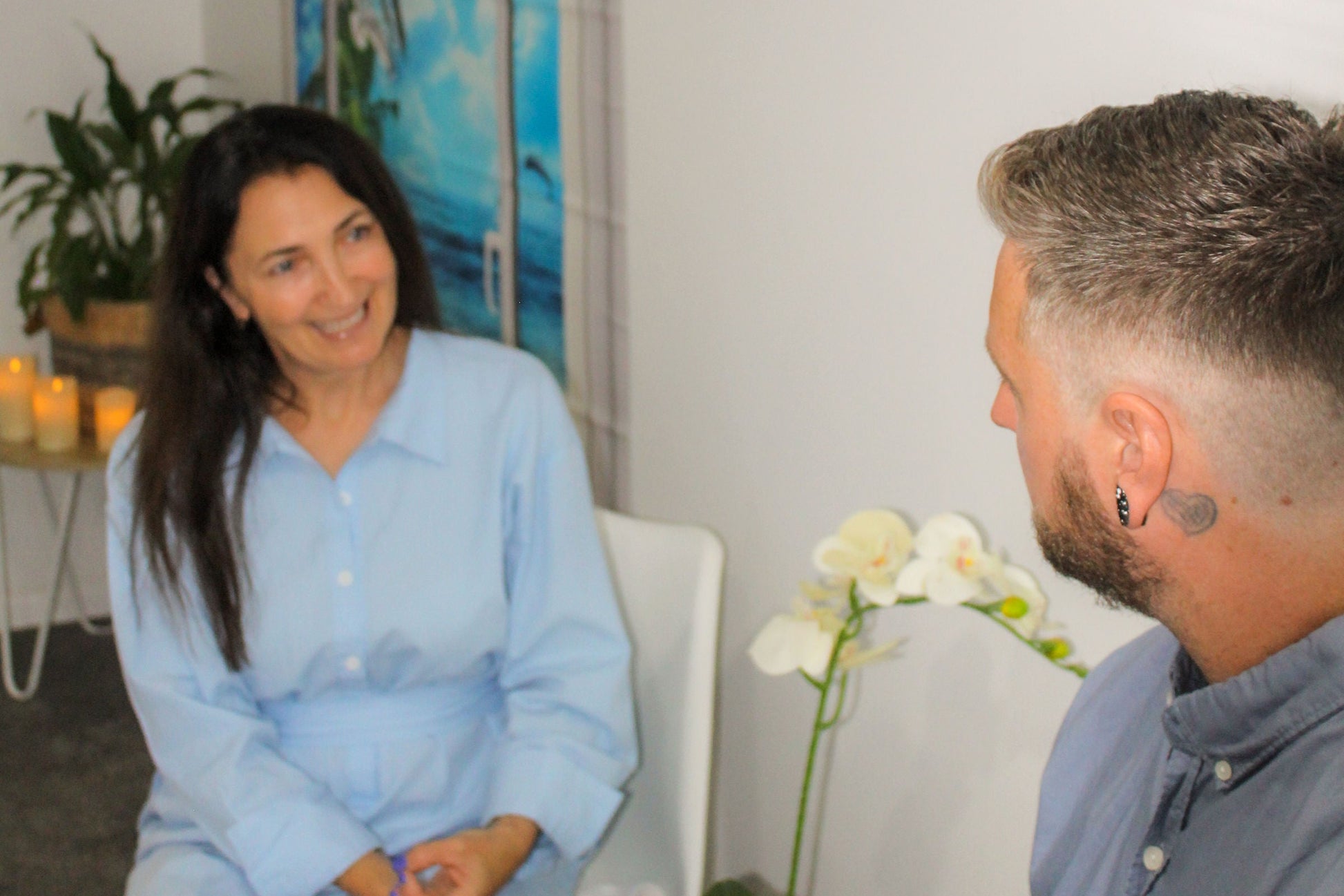 A staff member at Ocean Beach Oxygen in Tauranga, New Zealand, smiling while consulting with a male client. They are in a comfortable, clean therapy room.