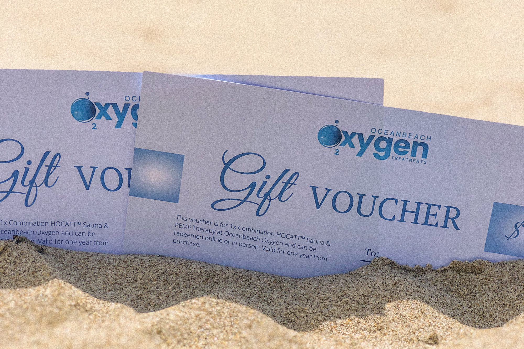 Oceanbeach Oxygen Treatments gift vouchers nestled in the sand, offering a unique gift of wellness with HOCATT sauna and PEMF therapy in Mount Maunganui.