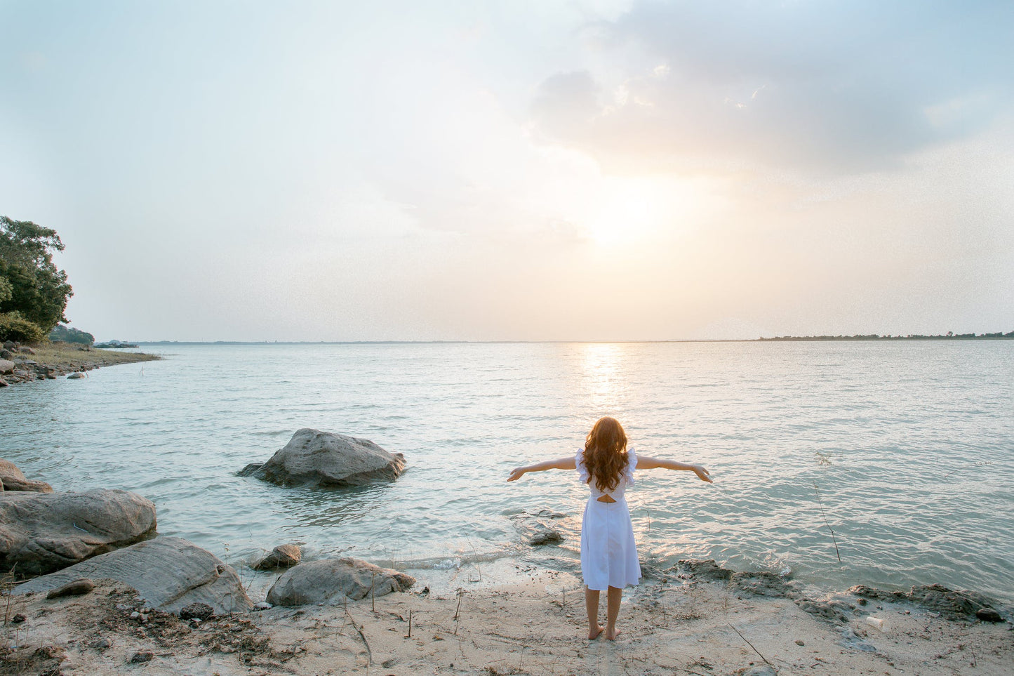 A woman stands on the ocean's edge with arms outstretched at sunset, symbolizing the renewed vitality and serenity that clients experience from HOCATT sauna and PEMF therapy at Oceanbeach Oxygen Treatments.
