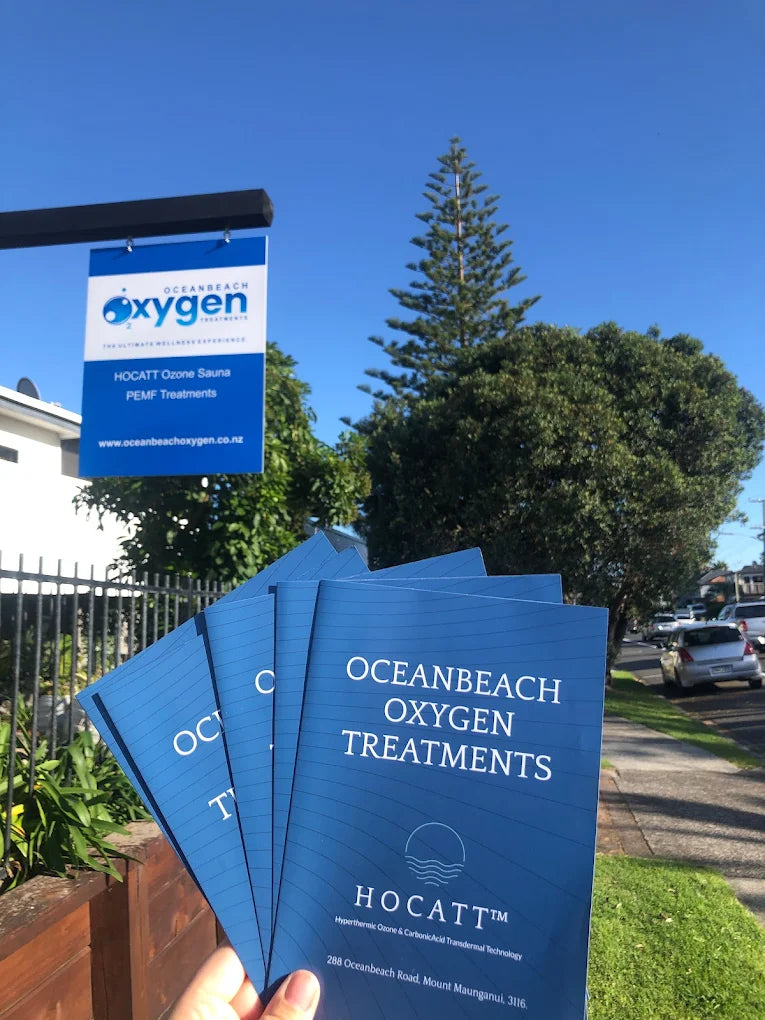 Blue pamphlets for Oceanbeach Oxygen Treatments held in front of a scenic background with trees and a clear sky.